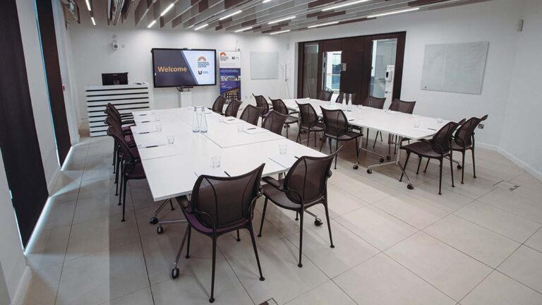 Seminar room set classroom-style with white tables and a welcome screen